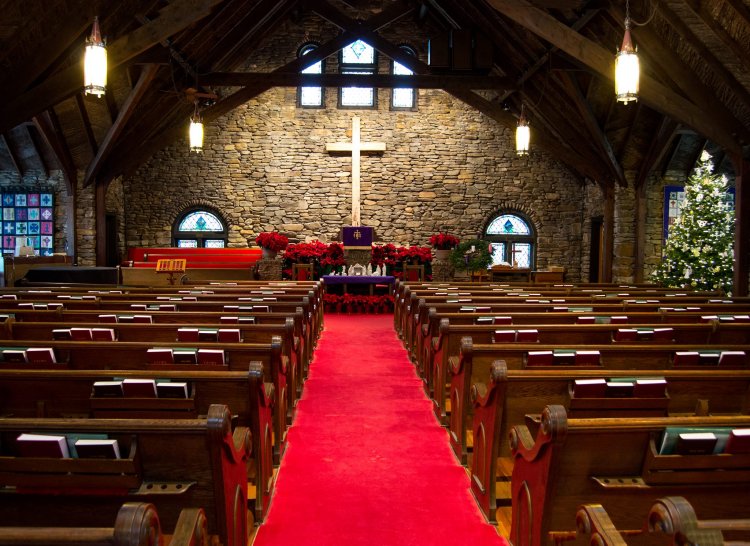 the interior of Crossnore Presbyterian's church sanctuary with rock walls, hardwood floors, red carpets, with huge ceiling beams